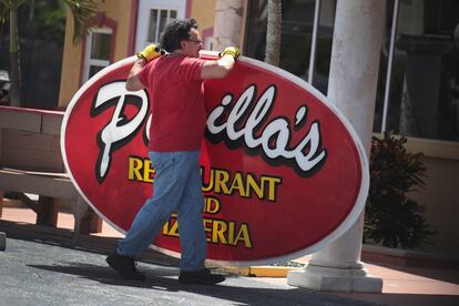 Un trabajador retira el cartel de un restaurante ante la llegada del huracán Dorian en Indialantic, Florida.