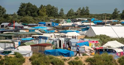 Migrantes caminan por 'La Jungla', el campo de refugiados de Calais (Francia) que el Gobierno de François Hollande quiere desmantelar. Más de 9.000 migrantes esperan en este reducto a dar el salto a Reino Unido escondidos como polizones en un barco que les lleve a las costas de Dover.