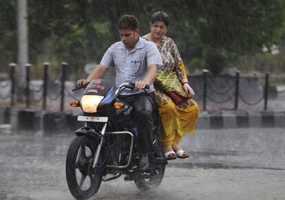 Una pareja india montados en una moto, bajo la lluvia en Jammu, India,