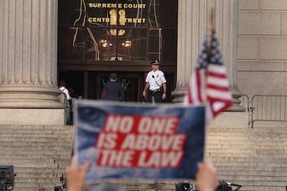 A protester holds a banner outside the gates of the New York courthouse where Trump testifies on Monday.