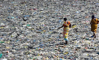 Dos mujeres caminan entre plásticos devueltos por el mar en la barriada de Colaba, en Mumbai (India), en mayo de 2020.