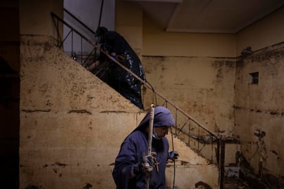 La casa de los padres de María José y Maite Miravet, ubicada en la calle Lepanto de Paiporta, muestra las huellas del barro tras la inundación del 29 de octubre. En la imagen, tomada el 12 de noviembre, unas monjas voluntarias participan en las tareas de limpieza, utilizando una hidrolimpiadora para retirar las marcas del lodo en las paredes y la escalera. La escena, bañada por la luz de tungsteno del interior, contrasta con el azul de los hábitos de las religiosas, aportando un toque de calidez a la habitación vacía. 