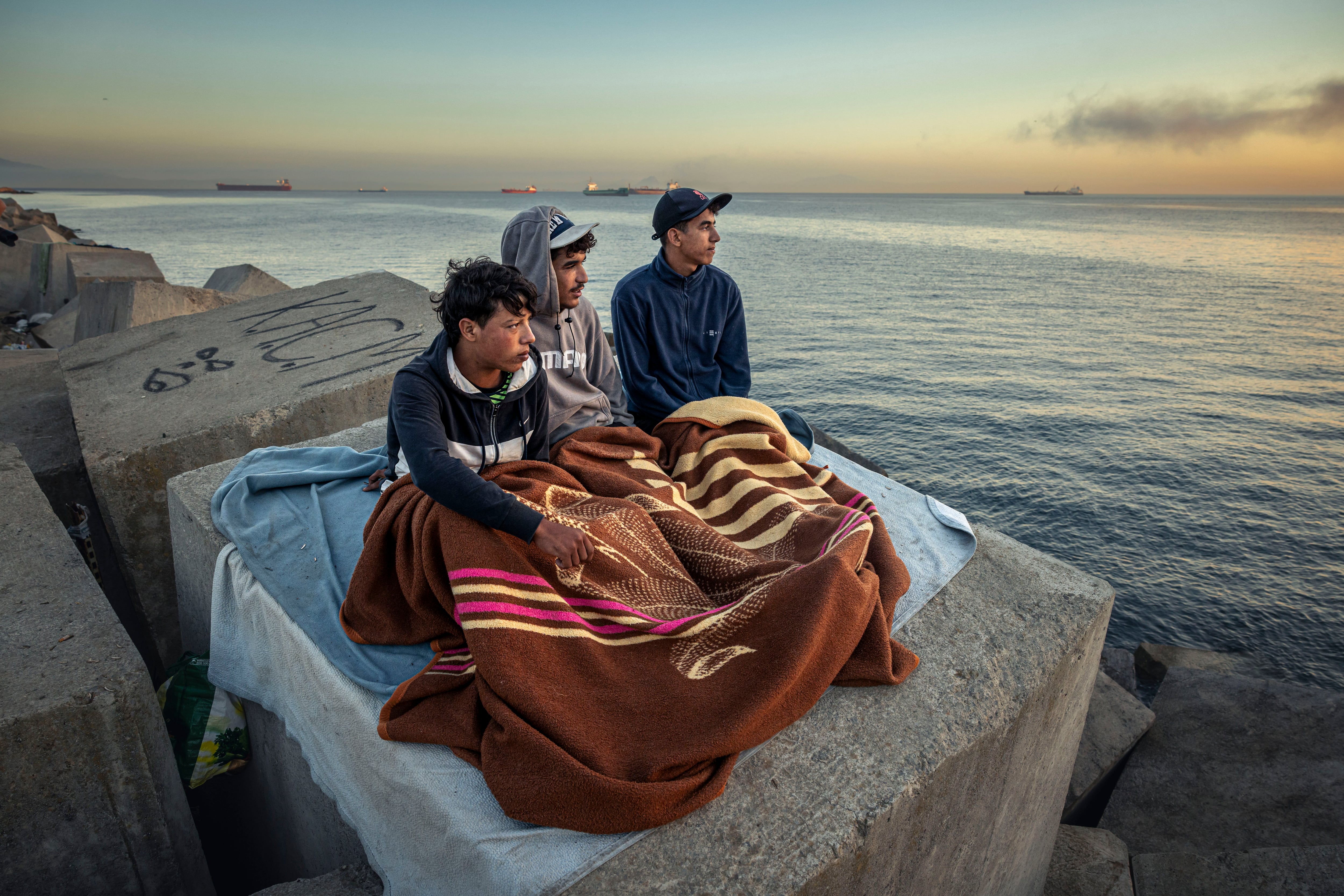 Unos migrantes que viven en la playa Benítez, a la espera del nuevo campamento temporal del muelle de Poniente del puerto de Ceuta , este miércoles. 