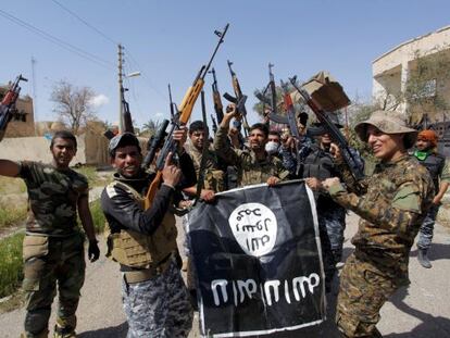 Un grupo de soldados y paramilitares sostiene una bandera del Estado Isl&aacute;mico arrebatada a los yihadistas durante la ofensiva de Tikrit.