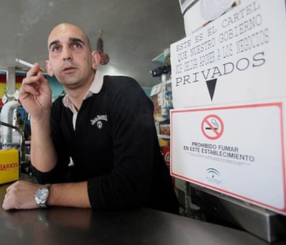 Rafael León, propietario del local sancionado en Cabra (Córdoba) por dejar fumar en su establecimiento hotelero, consume un cigarrillo junto a un cartel oficial que prohíbe fumar y otro de protesta.