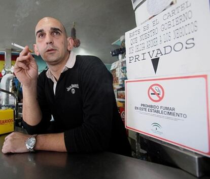 Rafael León, propietario del local sancionado en Cabra (Córdoba) por dejar fumar en su establecimiento hotelero, consume un cigarrillo junto a un cartel oficial que prohíbe fumar y otro de protesta.