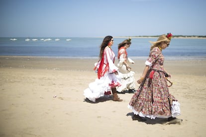 Tres mujeres vestidas de rociera, se acercan por la playa a uno de los barcos para cruzar a Doñana.