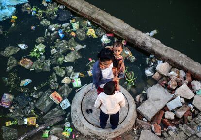 Tres personas frente a su residencia inundada por la subida del nivel del agua de los ríos Ganges y Yamunan en el área de Nagar del Allahabad (India), el 15 de septiembre de 2019.