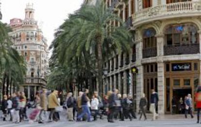 Numerosos peatones cruzan un paso de cebra situado ante la central en Valencia de La Caixa, ahora CaixaBank, mientras al fondo se ve el edificio del Banco de Valencia. EFE/Archivo