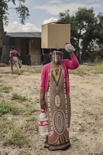 Una mujer de Nigeria porta una caja de alimentos, agua y equipos de protección contra la COVID 19 donados por distintas entidades sociales y ONG en un asentamiento de temporeros en Lucena del Puerto (Huelva).