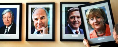 La empleada de un pub berlinés cuelga la foto de Merkel tras ser elegida en 2005, junto a las de  Schmidt,  Kohl y Schröder.