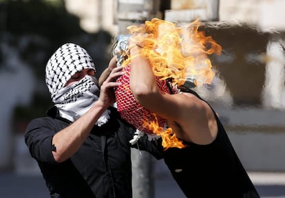 Un palestino intenta ayudar a un compañero que se ha prendido fuego al lanzar un cóctel molotov contra soldados israelís durante una protesta en Hebrón (Palestina).