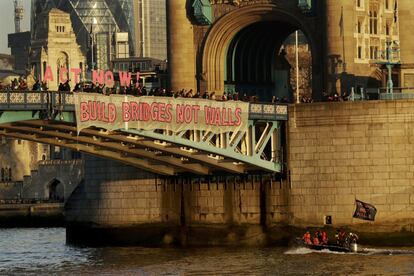 Un lancha cruza el Puente de la Torre de Londres (Inglaterra) mientras un grupo de manifestantes muestran una pancarta donde se lee: "Construye puentes, no muros".