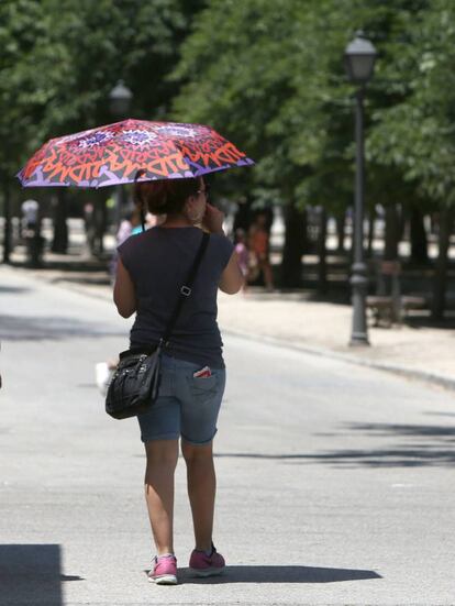 Una mujer camina con un paraguas para protegerse del sol en el Parque de El Retiro.