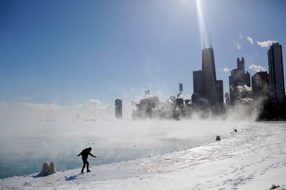 Una mujer camina cerca del lago Míchigan helado con Chicago al fondo.