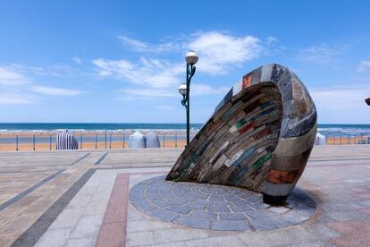 El verano zarautzarra es sinónimo de centenares de toldos en los que alternan rayas blancas con azules o verdes, diseño con el que la artista Maite Isasti ha creado mascarillas. Esta línea alegre y colorista de casetas se estiliza a lo largo del arenal más extenso de Gipuzkoa. Una estampa mítica, tanto que Karlos Arguiñano creó el 'pintxo' Toldotxo con merluza y pimiento verde, que puede degustarse en muchos bares de Zarautz. <BR></BR>En la imagen, 'Joan etorrian', de Miguel Angel Lertxundi, frente a la playa de Zarautz.