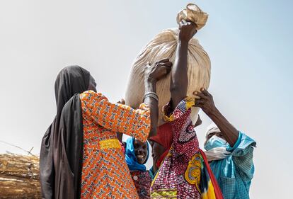 Dos mujeres y un hombre ayudan a otro refugiado a recoger una bolsa de grano en la distribución de alimentos.