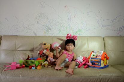 Jiang Siqi posa en el sofá del piso en el que vive la familia con algunos de sus juguetes y bajo los borrones que ha ido haciendo en la pared junto a su hermana mayor.
