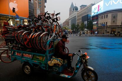 Un hombre monta en un triciclo que transporta bicicletas compartidas cerca de la calle Wangfujing, en Pekín (China).