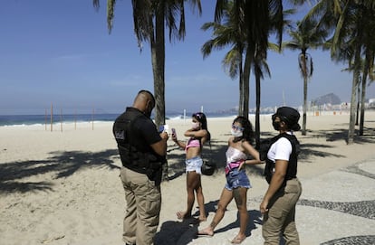 Dos policías municipales ponen una multa a dos mujeres que no llevaban mascarilla en la playa de Leme en Río de Janeiro, este sábado. Durante este fin de semana no está permitido permanecer en la arena, tomarse un baño o realizar deporte, medida que se une a otras impuestas anteriormente para intentar reducir la propagación del virus.