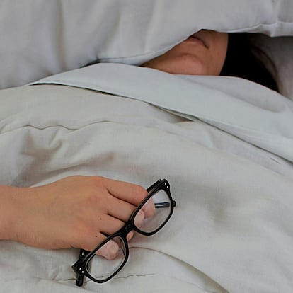 Chica durmiendo en una cama con unas gafas en la mano