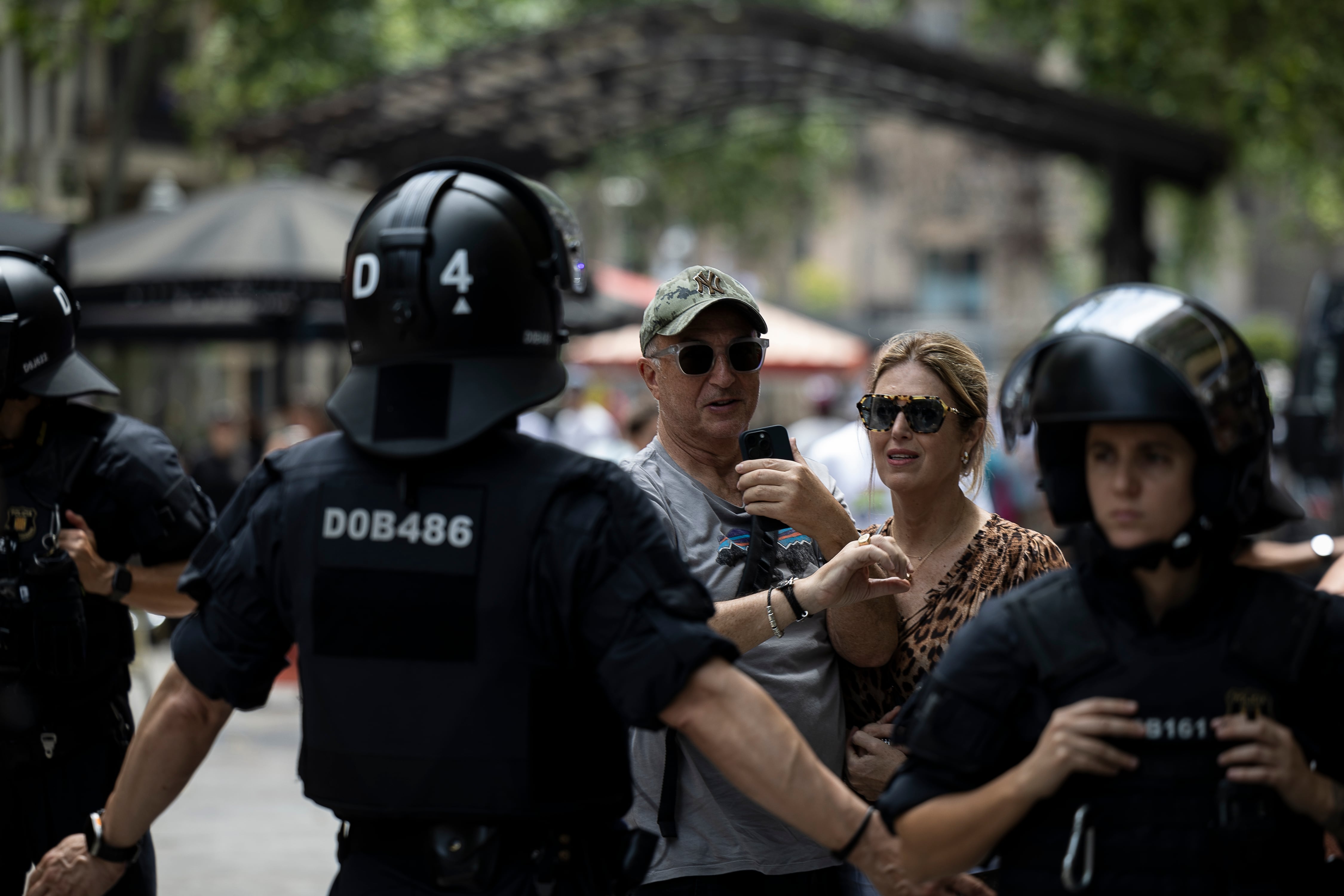 Agentes de los Mossos d’Escuadra apartan a una pareja de turistas de las proximidades de la manifestación en la avenida de Gaudí en Barcelona, este domingo.