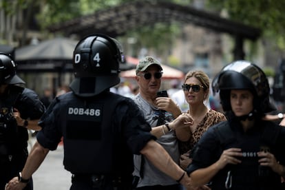 Agentes de los Mossos d’Escuadra apartan a una pareja de turistas de las proximidades de la manifestación en la avenida de Gaudí en Barcelona, este domingo.