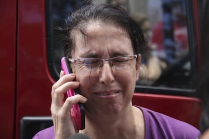 Mulher fala ao telefone enquanto aguarda informações em frente a escola