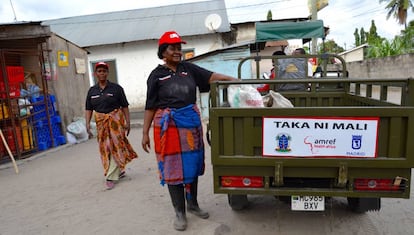 Dos mujeres de Taka Ni Mali depositan la basura en el carromato para su traslado.