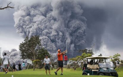 Un grupo de gente juega al golf frente a una columna de humo y ceniza proveniente del volcán Kilauea en la isla grande de Hawái, el 15 de mayo de 2018.