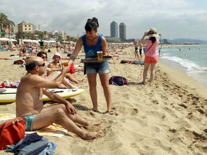 Una camarera de uno de los chiringuitos de la playa de Sant Sebasti&agrave; atiende a un ba&ntilde;ista pocos metros del mar.