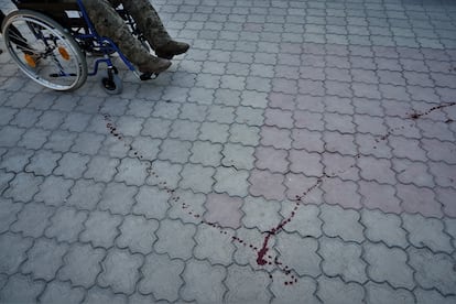 Un militar herido leve es trasladado en silla de ruedas sobre el reguero de sangre dejado por otro compañero.