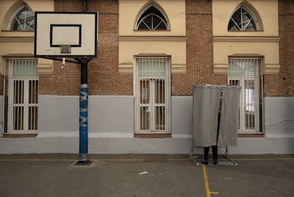 Una mujer prepara su voto tras una cortinilla situada junto a una canasta ubicada en el patio de un colegio electoral de Madrid.