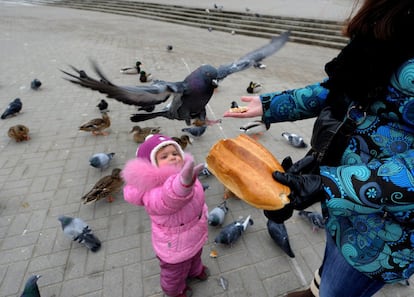 Una niña alimenta a unas palomas junto a su madre en Minsk (Bielorrusia).