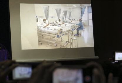 Profissionais de imprensa tentam fotografar uma tela do hospital em que uma imagem das crianças resgatadas é projetada.