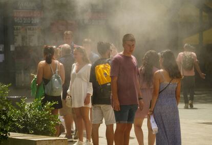Varias personas se refugian del calor bajo unos vaporizadores de agua, este jueves en Valencia.