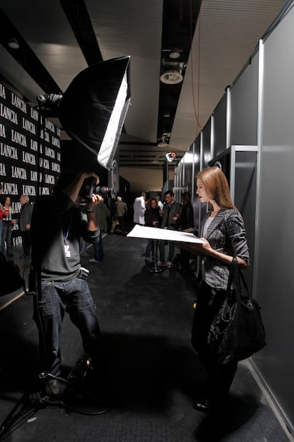 Una modelo posa ante un fotógrafo en el <i>backstage</i>. También se han visto trajes de chaqueta vaporosos y fluídos tipo años setenta, colores retro y brocados muy trabajados.