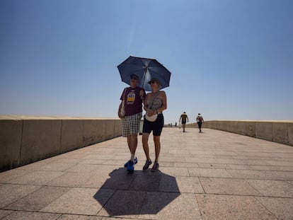 Una pareja de turistas caminan bajo un paraguas para paliar los rayos de sol, este lunes por el Puente Romano de Córdoba.