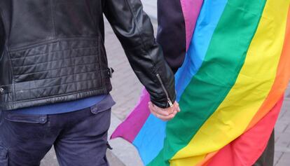 Foto de archivo donde una pareja se coge la mano con la bandera multicolor.