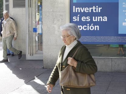 Varios peatones pasan delante de una oficina bancaria con publicidad de planes de pensiones.