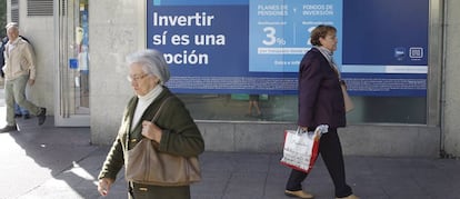 Varios peatones pasan delante de una oficina bancaria con publicidad de planes de pensiones.