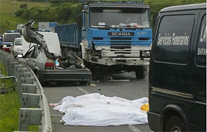 El turismo siniestrado en Abanto, junto al camión con el que colisionó y los cadáveres de los fallecidos cubiertos con sábanas.