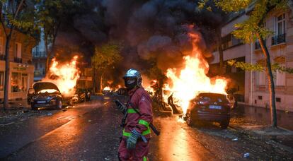 Un bombero junto a varios vehículos ardiendo en París.