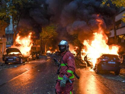 Un bombero junto a varios vehículos ardiendo en París.