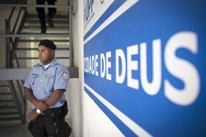 Policial de guarda em frente ao cartaz da Unidade de Polícia Pacificadora (UPP) de Cidade de Deus.