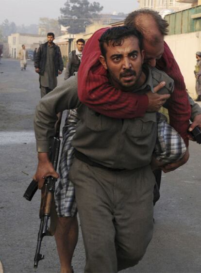 Un policía afgano acarrea a un herido en el asalto a la pensión donde se aloja personal de la ONU.