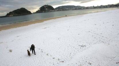 Un hombre pasea a su perro en la playa de Ondarreta de San Sebastián cubierta por la nieve.