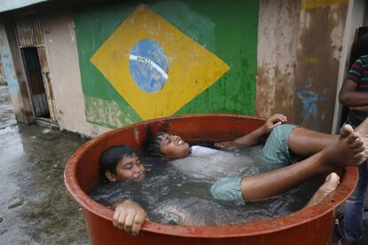 Unos niños se bañan en un tanque de agua, delante de una pintura de la pared con la bandera de 2014 sede de la Copa Mundial de Brasil, en Daca (Bangladés).