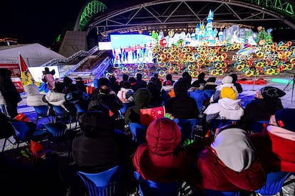 La gente mira una pantalla con imágenes en vivo de la ceremonia de apertura en el Centro Deportivo Olímpico Shenyang.