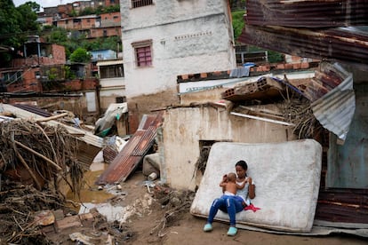 Una mujer sostiene a un bebé frente a su casa dañada por las inundaciones.